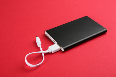 Photo of Modern portable charger with cable on red background