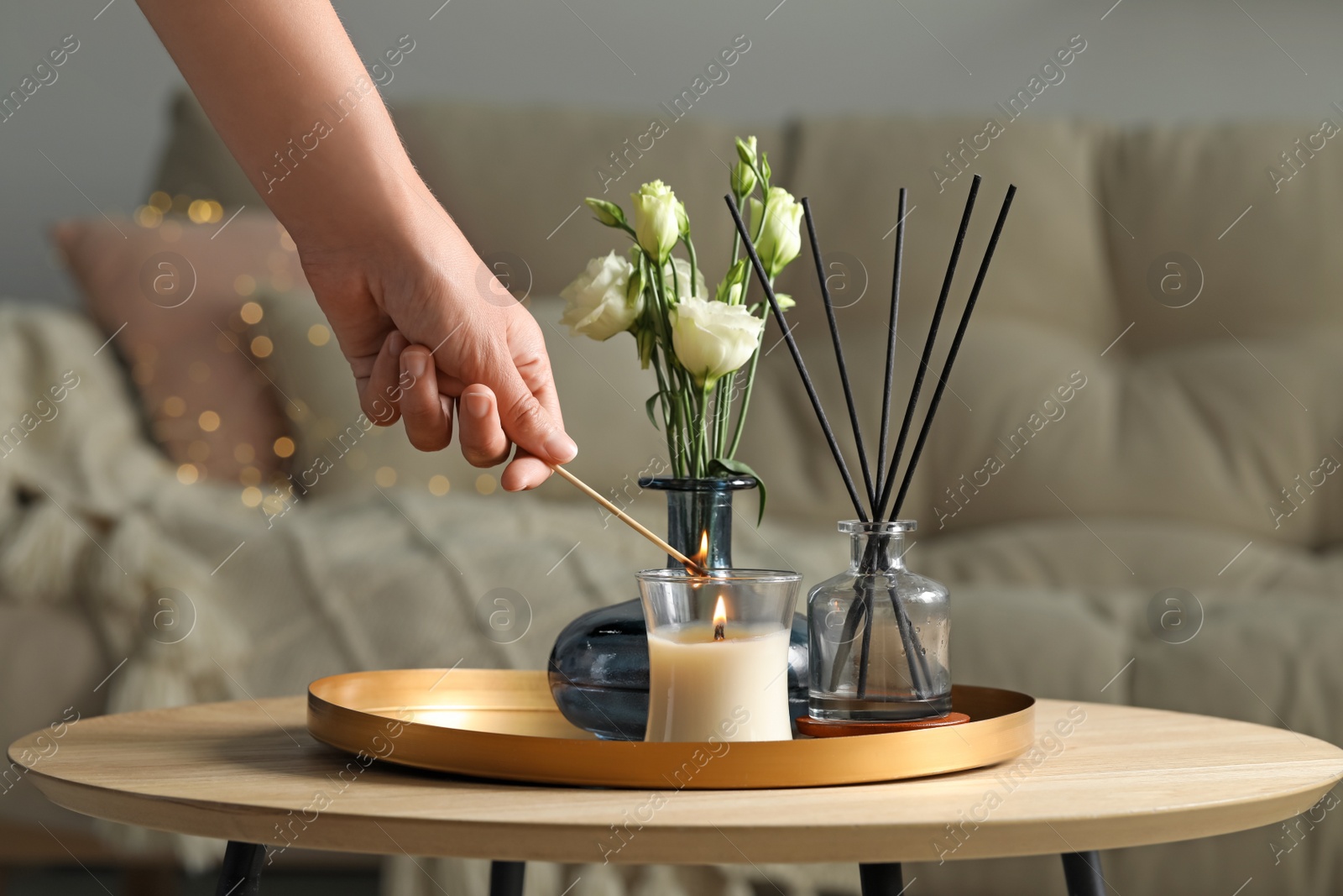 Photo of Woman lighting candle at wooden table in living room, closeup