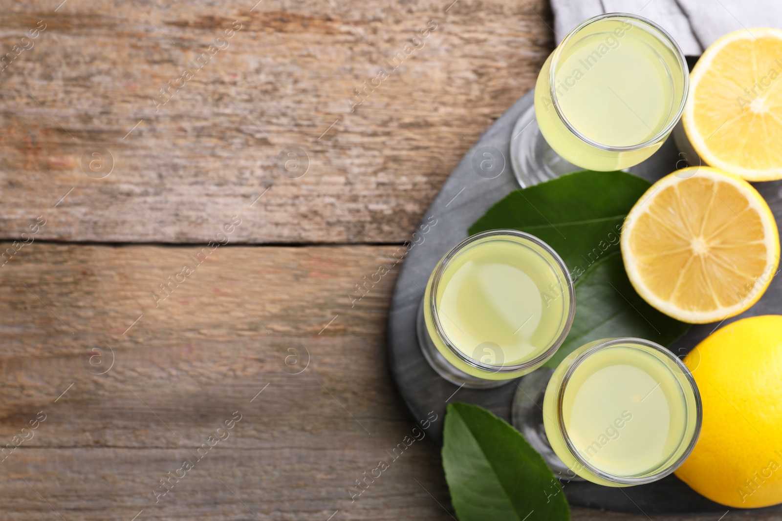 Photo of Tasty limoncello liqueur, lemons and green leaves on wooden table, top view. Space for text