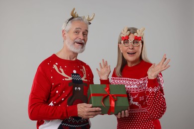 Photo of Couple in Christmas sweaters. Senior man presenting gift to his woman on grey background