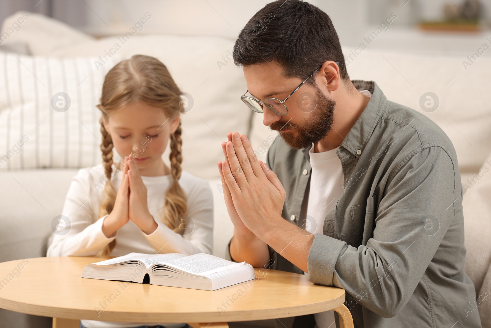 Photo of Girl and her godparent praying over Bible together at table indoors