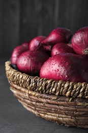 Photo of Wicker bowl of wet whole red onion bulbs on grey table, closeup