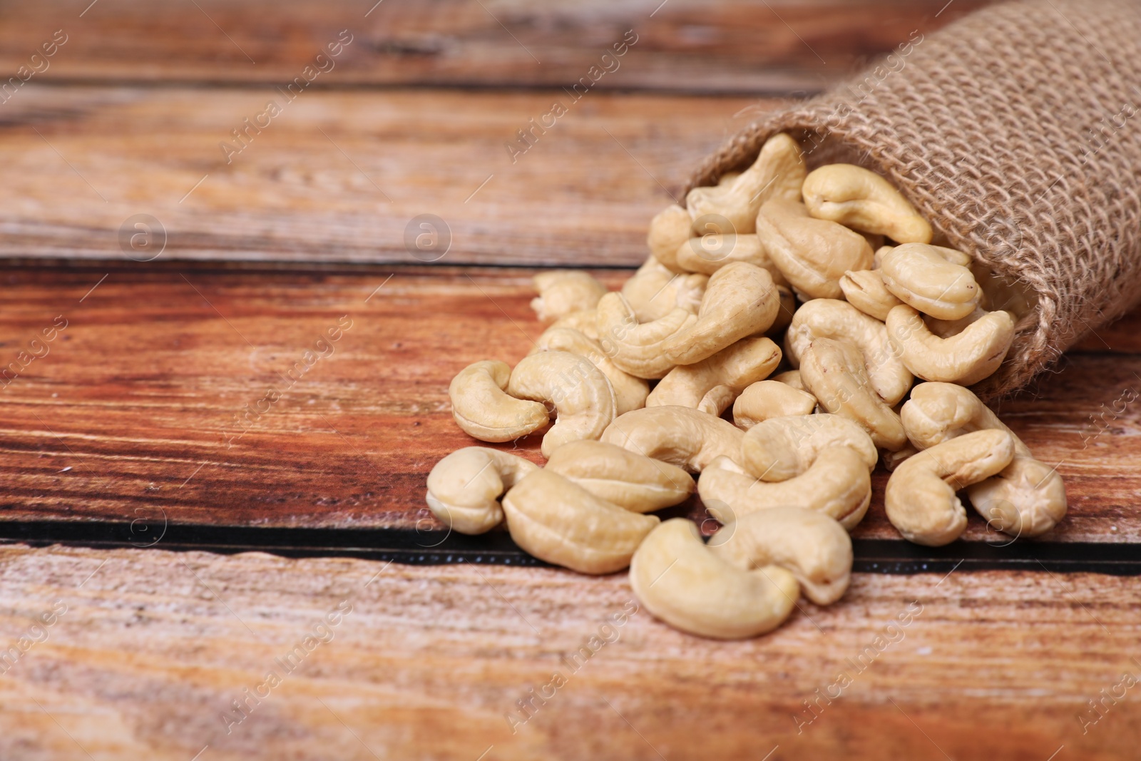 Photo of Sack with tasty cashew nuts on wooden table, closeup. Space for text