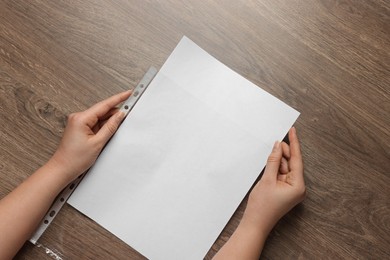 Photo of Woman putting paper sheet into punched pocket at wooden table, top view