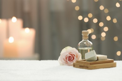 Beautiful spa composition with essential oil, soap bar and rose on white towel against blurred background. Space for text