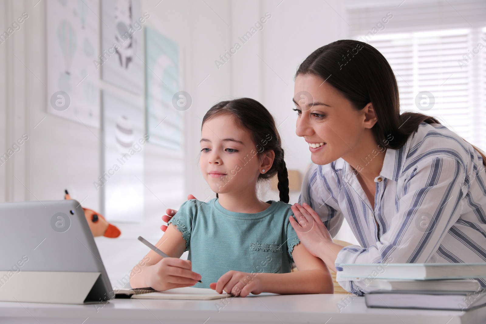 Photo of Mother helping her daughter doing homework with tablet at home