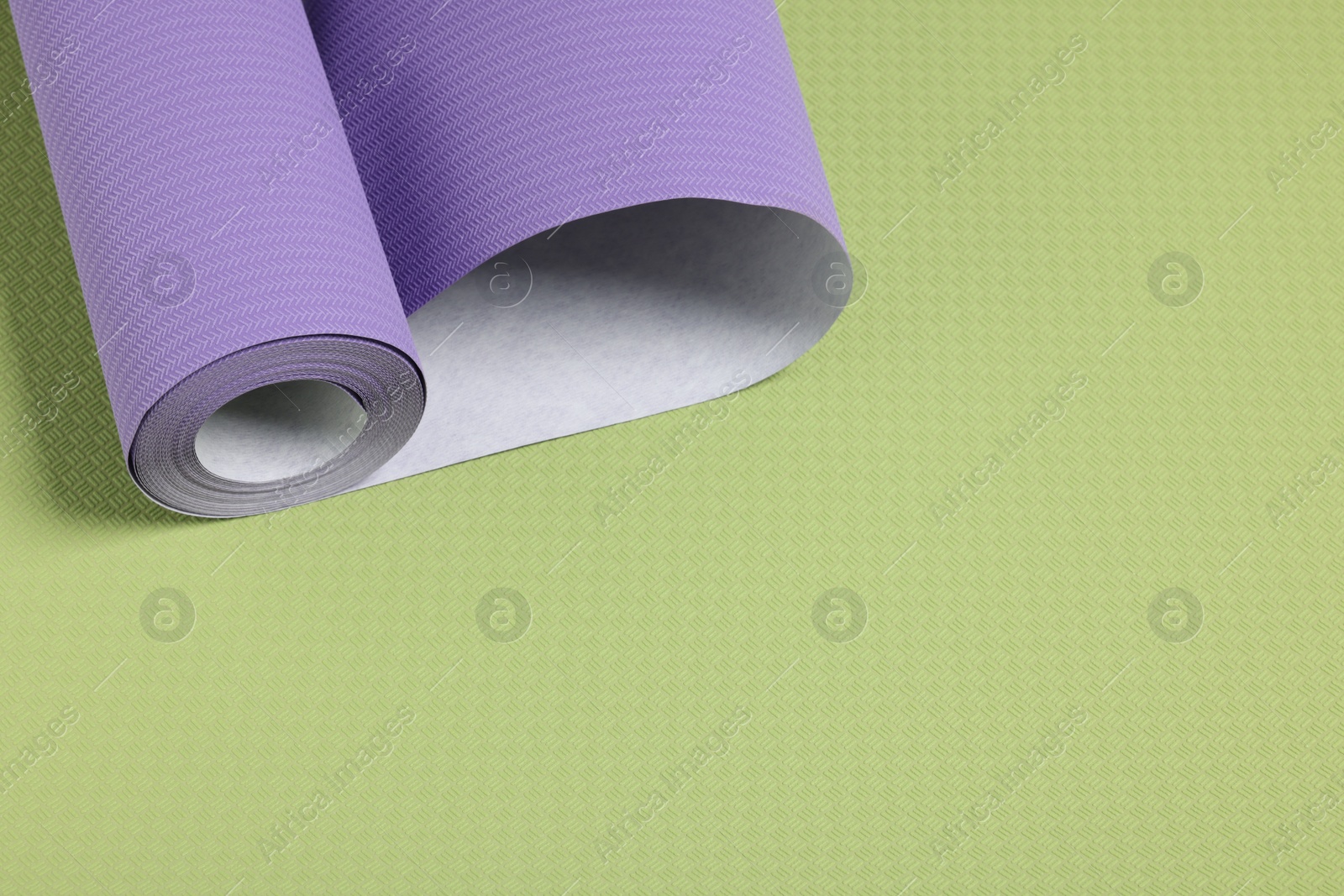 Photo of One violet wallpaper roll on green sample, space for text