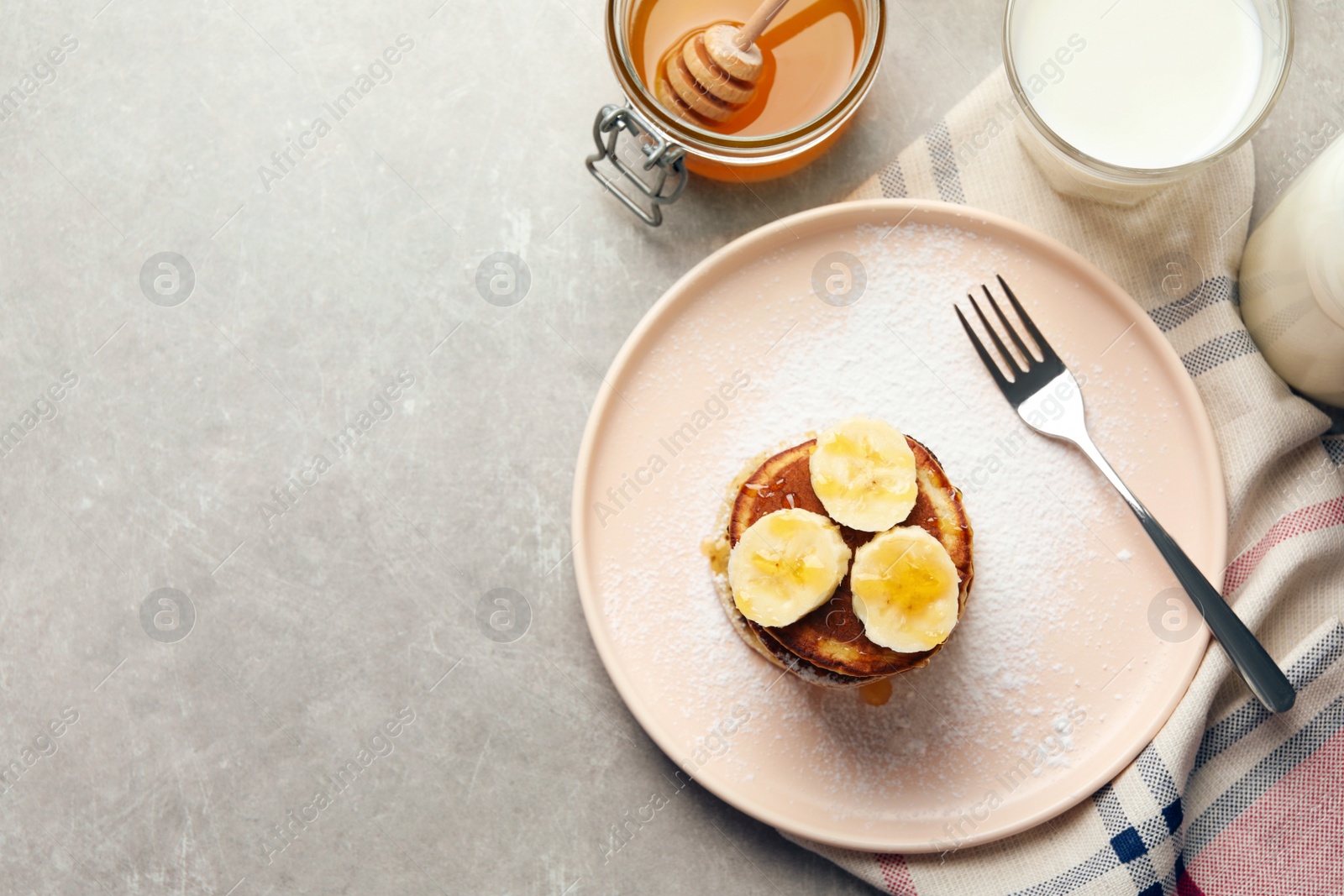 Photo of Plate of banana pancakes with honey and powdered sugar served on light grey table, flat lay. Space for text