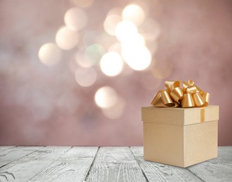 Beautiful gift box on white wooden table against blurred festive lights, bokeh effect. Space for text