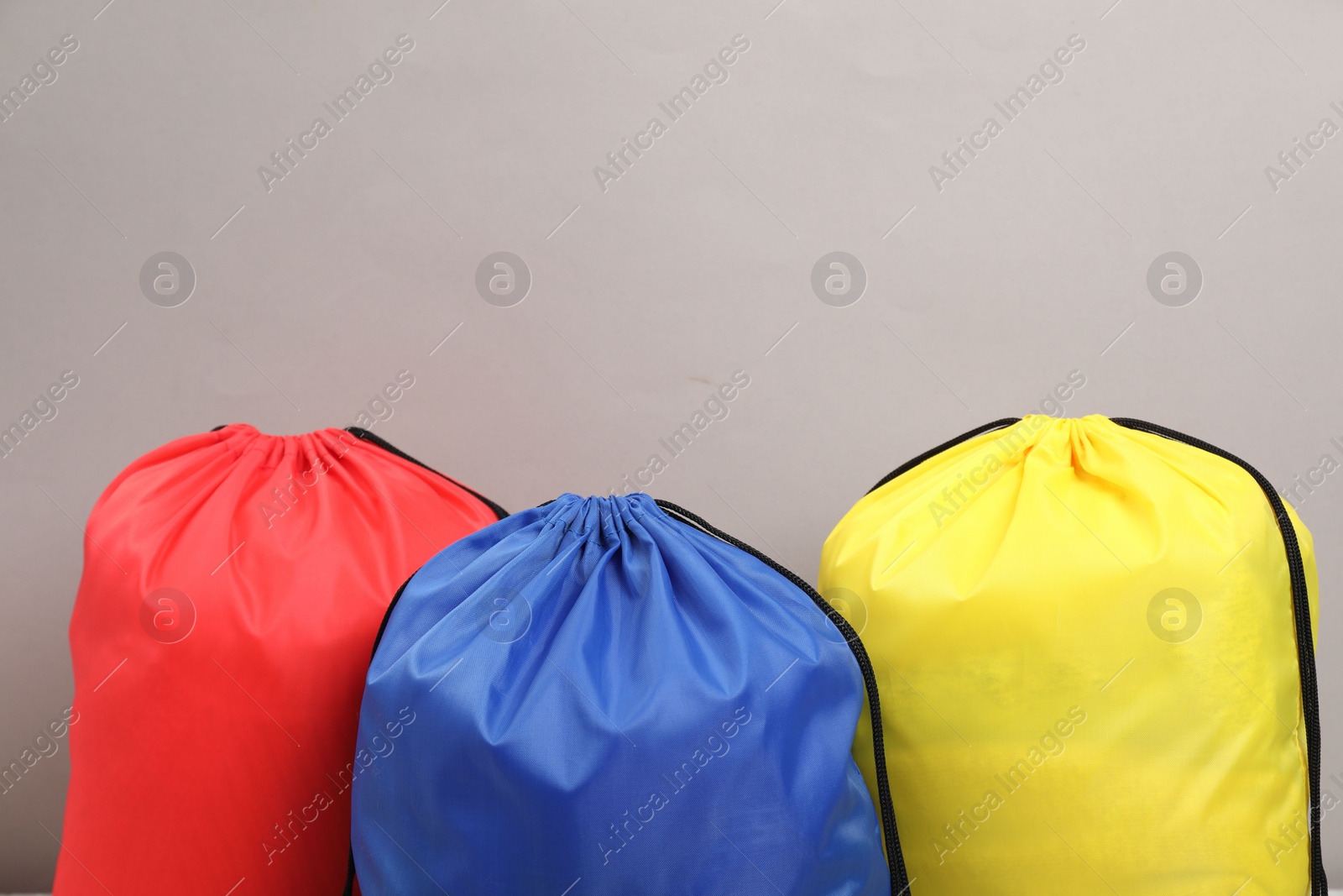 Photo of Three drawstring bags on grey background, closeup. Space for text