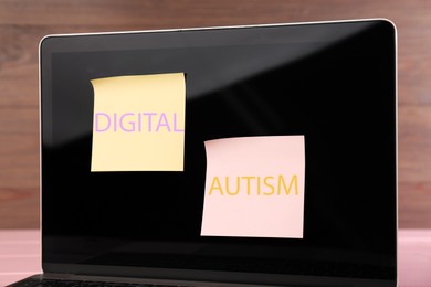 Photo of Sticky notes with phrase Digital Autism attached to laptop on table, closeup. Addictive behavior