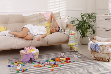 Photo of Tired young mother sleeping on sofa in messy living room