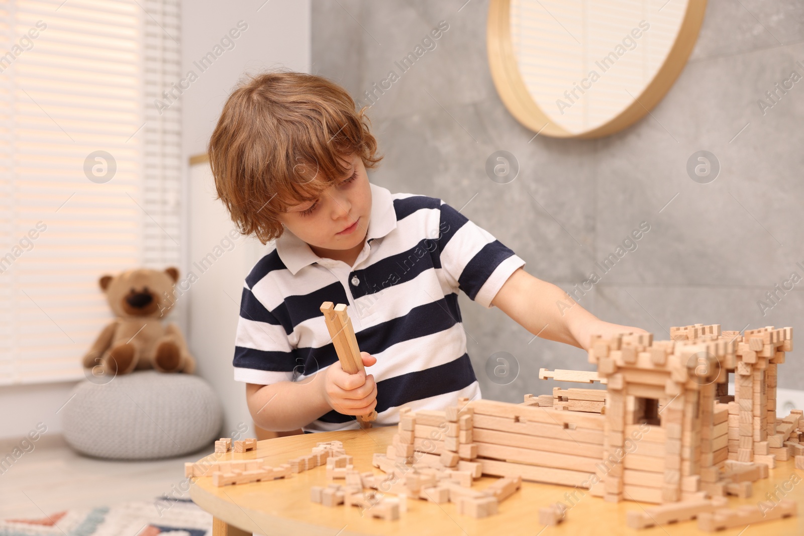 Photo of Little boy playing with wooden entry gate at table in room. Child's toy