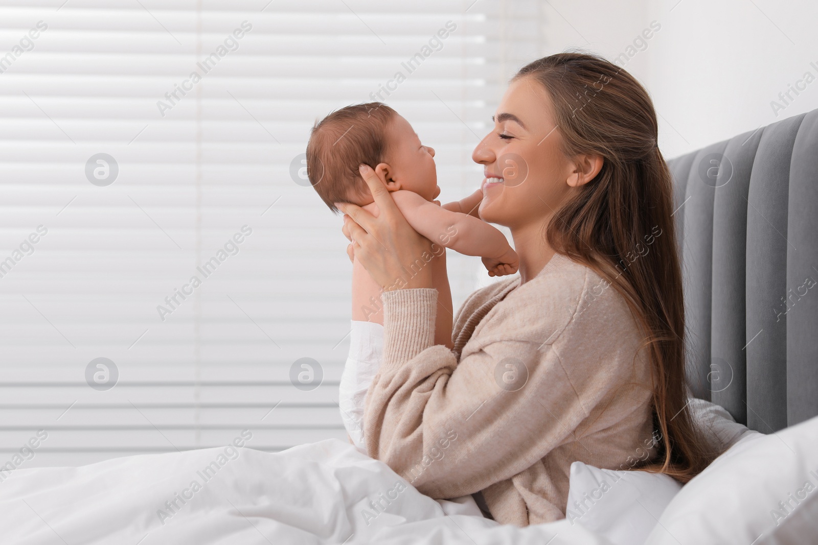 Photo of Mother holding her cute newborn baby in bed indoors, space for text