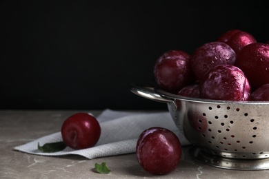 Photo of Delicious ripe plums in colander on grey marble table. Space for text