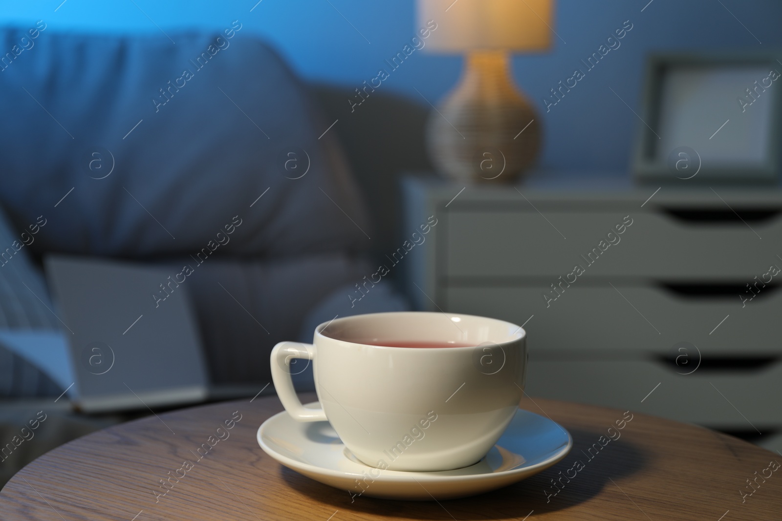 Photo of Cup of hot tea on wooden table at night