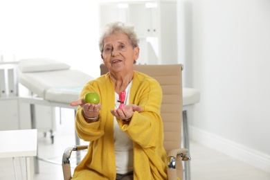 Photo of Senior woman with between apple and candy in hospital. Diabetes diet