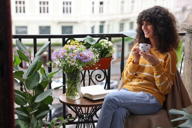 Photo of Young woman with cup of drink relaxing near green houseplants on balcony