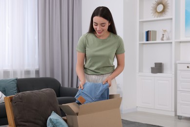 Photo of Happy young woman taking jeans out of box at home. Online shopping