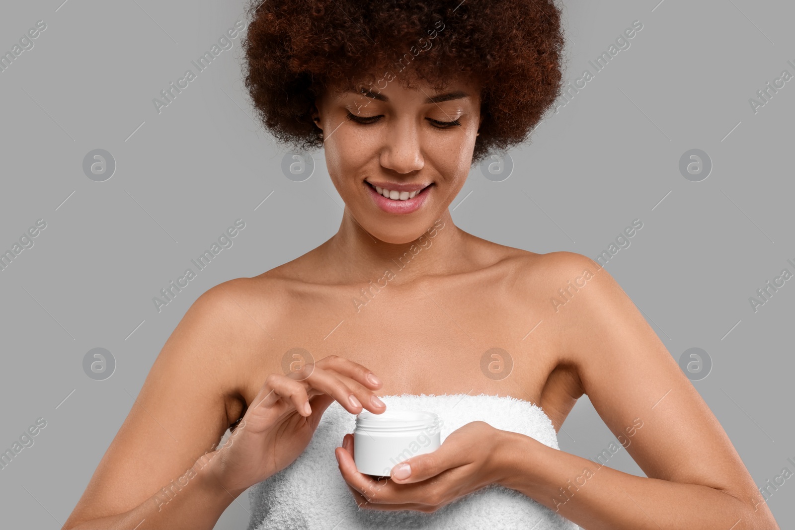 Photo of Beautiful young woman holding body cream on grey background