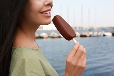 Photo of Young woman eating ice cream glazed in chocolate near river, closeup
