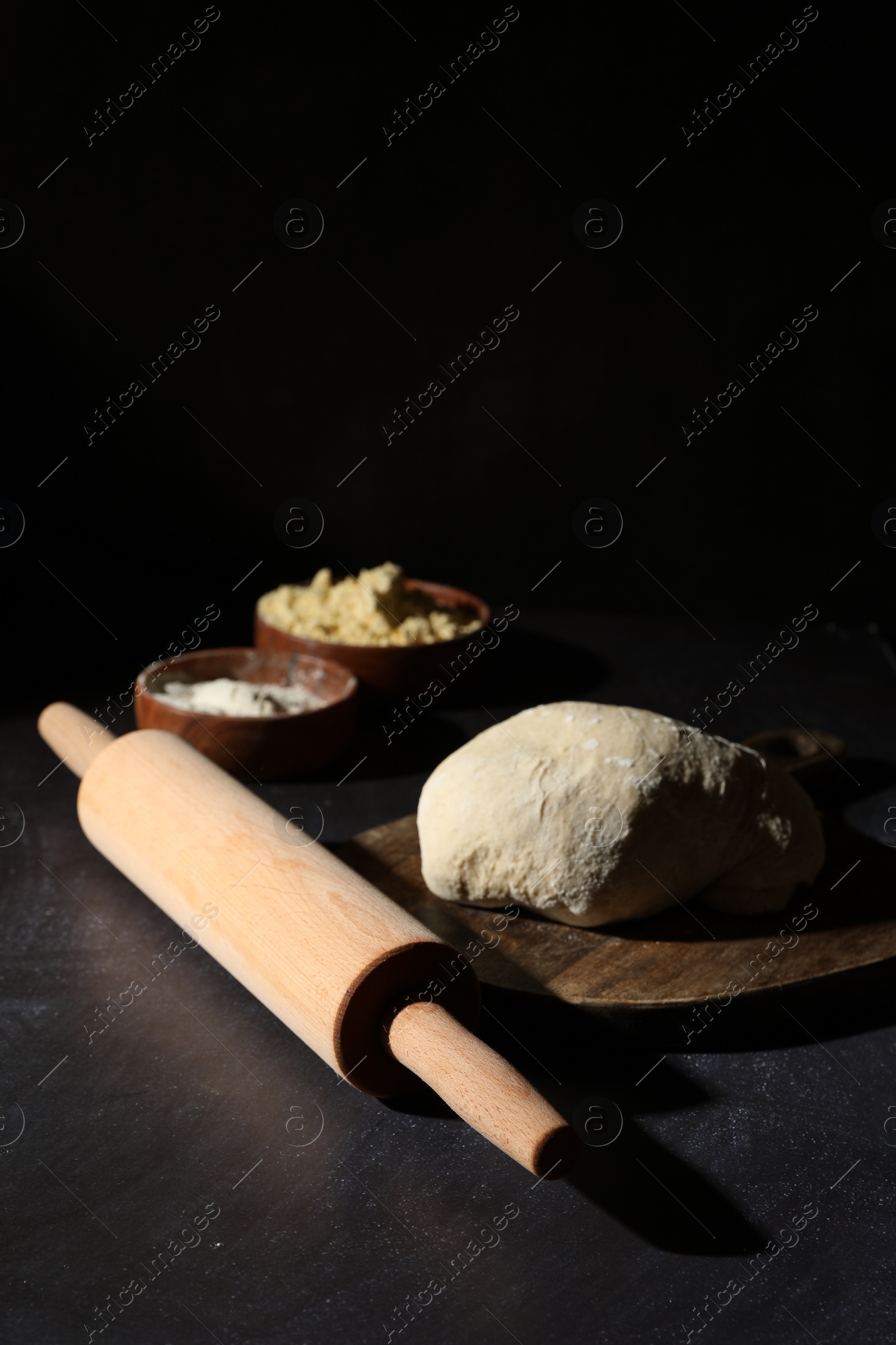 Photo of Rolling pin, flour and dough on black table