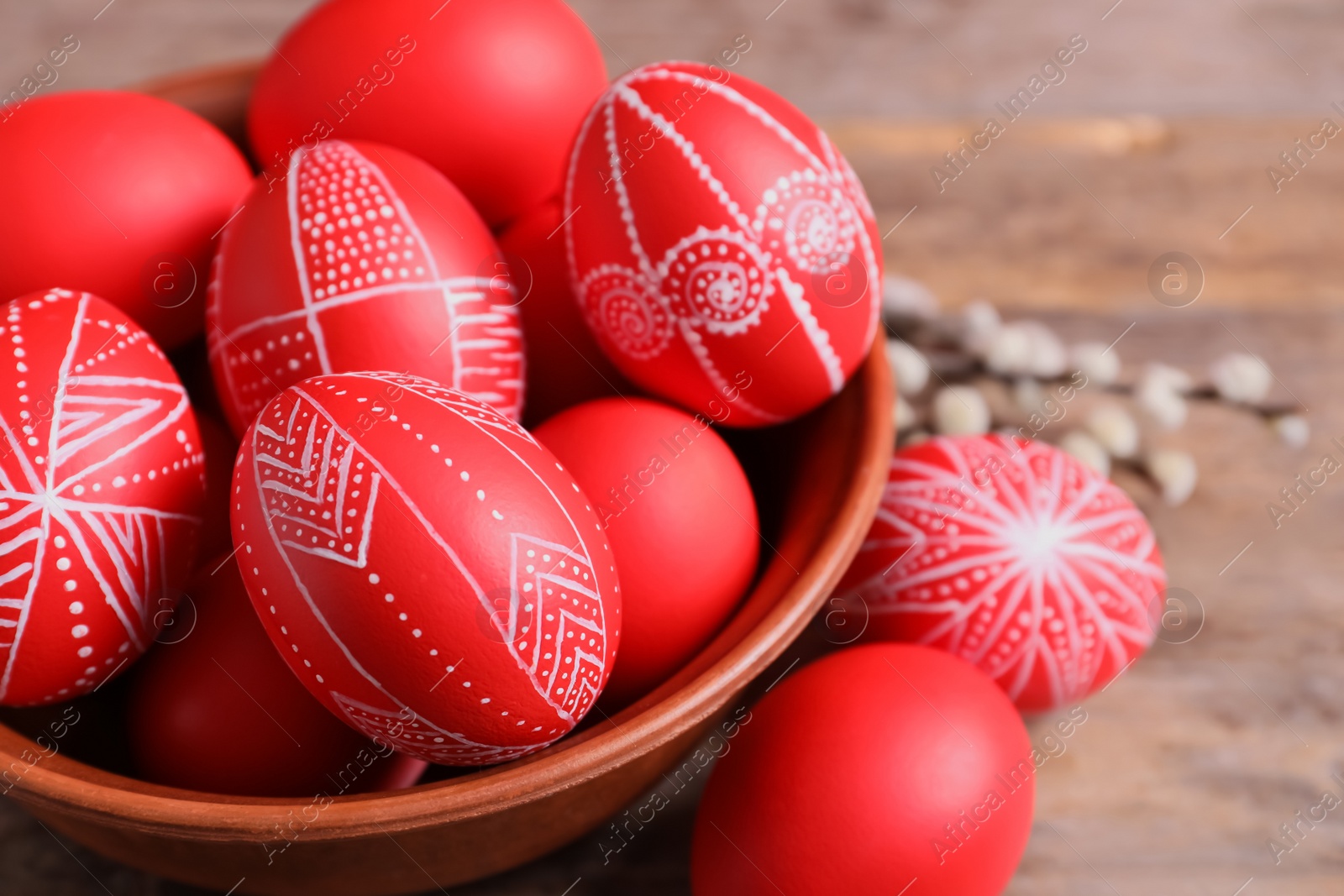 Photo of Wooden bowl with red painted Easter eggs on table, closeup