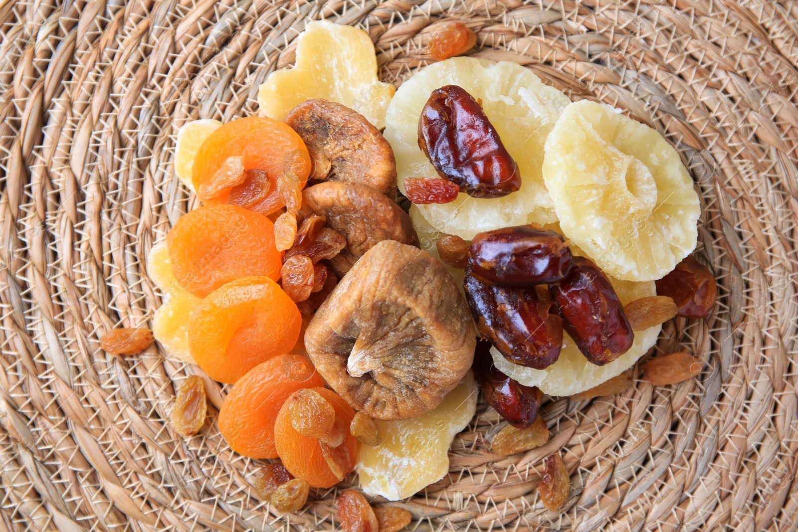 Photo of Pile of different tasty dried fruits on wicker mat, flat lay