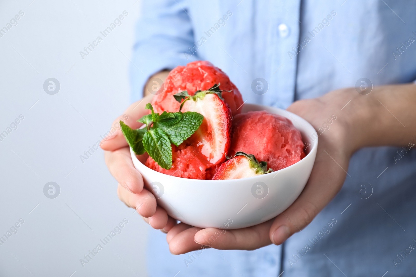 Photo of Woman holding bowl full of delicious ice cream and strawberries on light grey background, closeup. Space for text