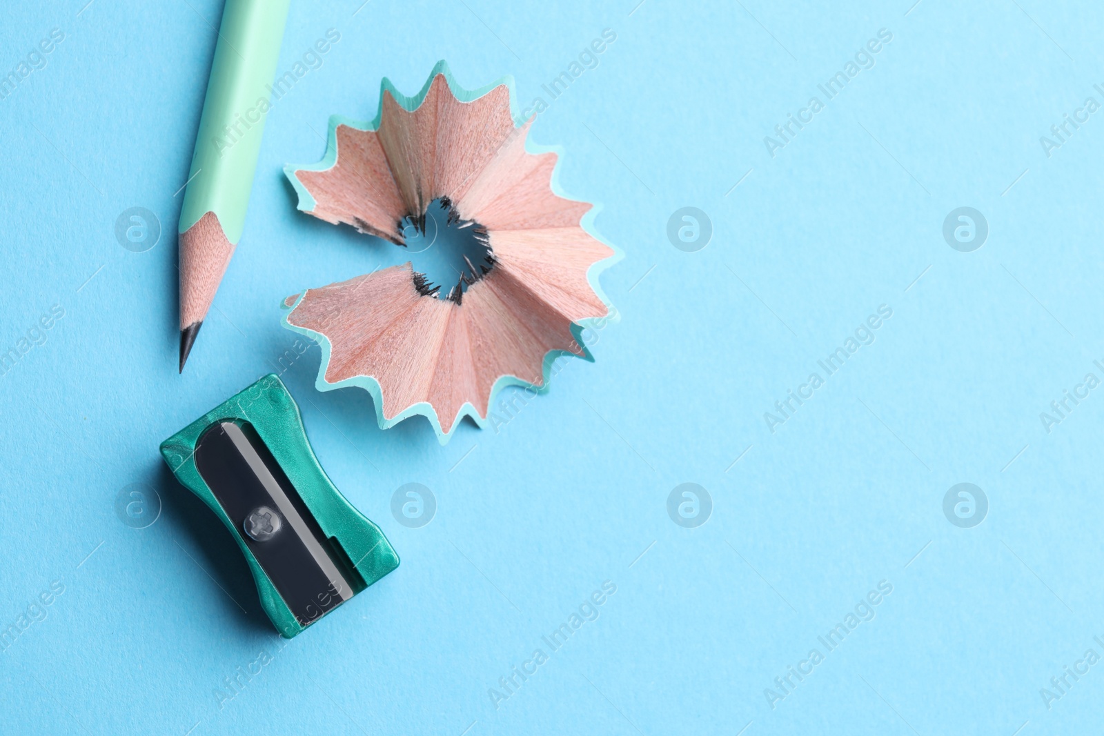 Photo of Pencil, sharpener and shavings on light blue background, flat lay. Space for text