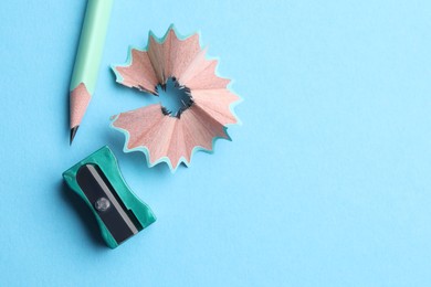Photo of Pencil, sharpener and shavings on light blue background, flat lay. Space for text