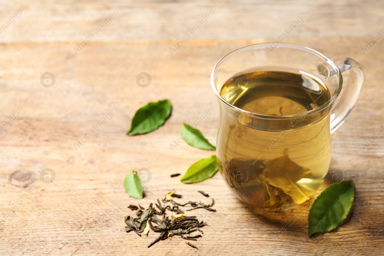 Photo of Cup of green tea, dry and fresh leaves on wooden table. Space for text 