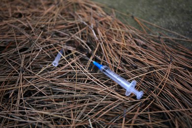 Disposable syringe with needle on heap of dry branches