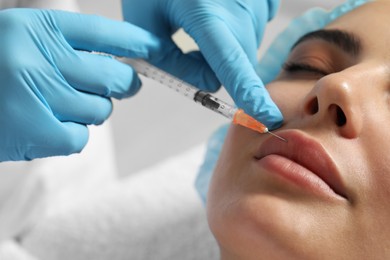Photo of Doctor giving lips injection to young woman in clinic, closeup. Cosmetic surgery