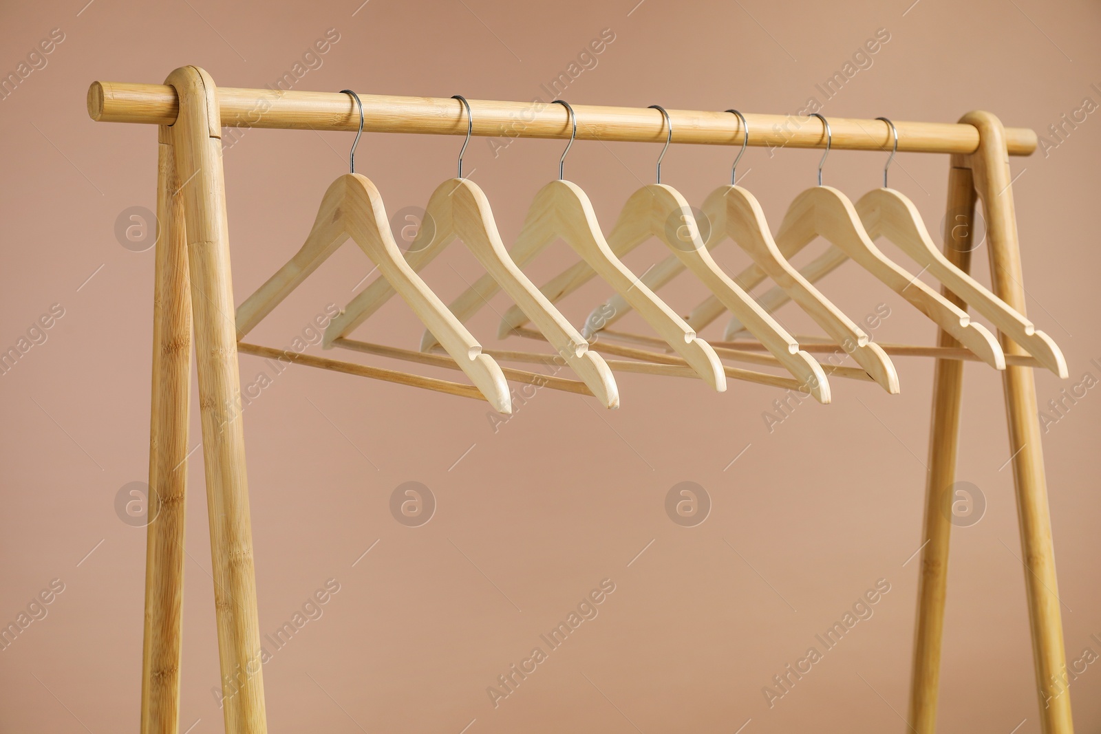 Photo of Empty clothes hangers on wooden rack against light brown background