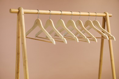 Photo of Empty clothes hangers on wooden rack against light brown background