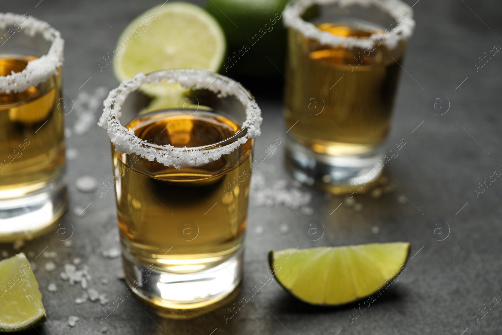 Photo of Mexican Tequila shots, lime slices and salt on grey table