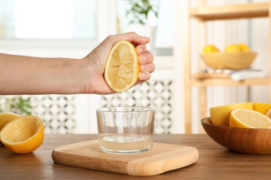 Photo of Woman squeezing lemon juice into glass bowl at table