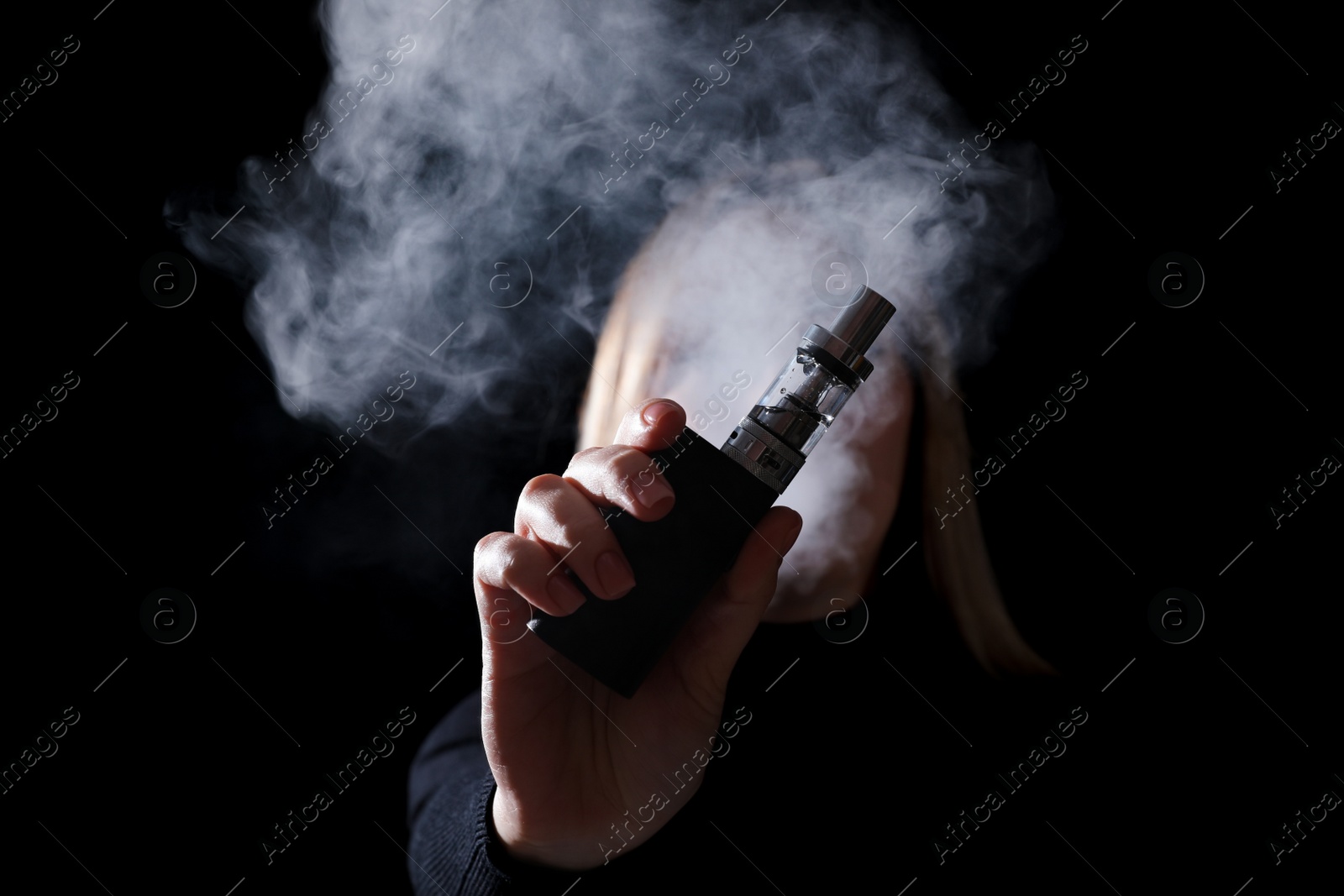 Photo of Young woman holding electronic cigarette against black background, focus on hand