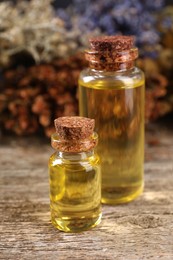 Bottles of essential oils and many different dry herbs on wooden table, closeup