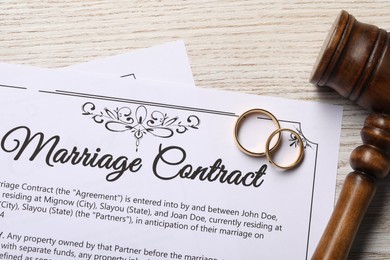 Photo of Marriage contract, golden wedding rings and gavel on wooden table, top view