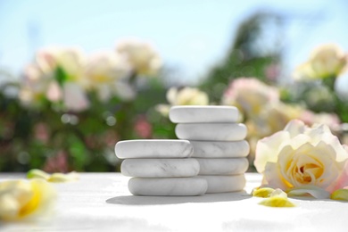Photo of Stack of spa stones and beautiful rose on white table in blooming garden, space for text. Harmony and zen