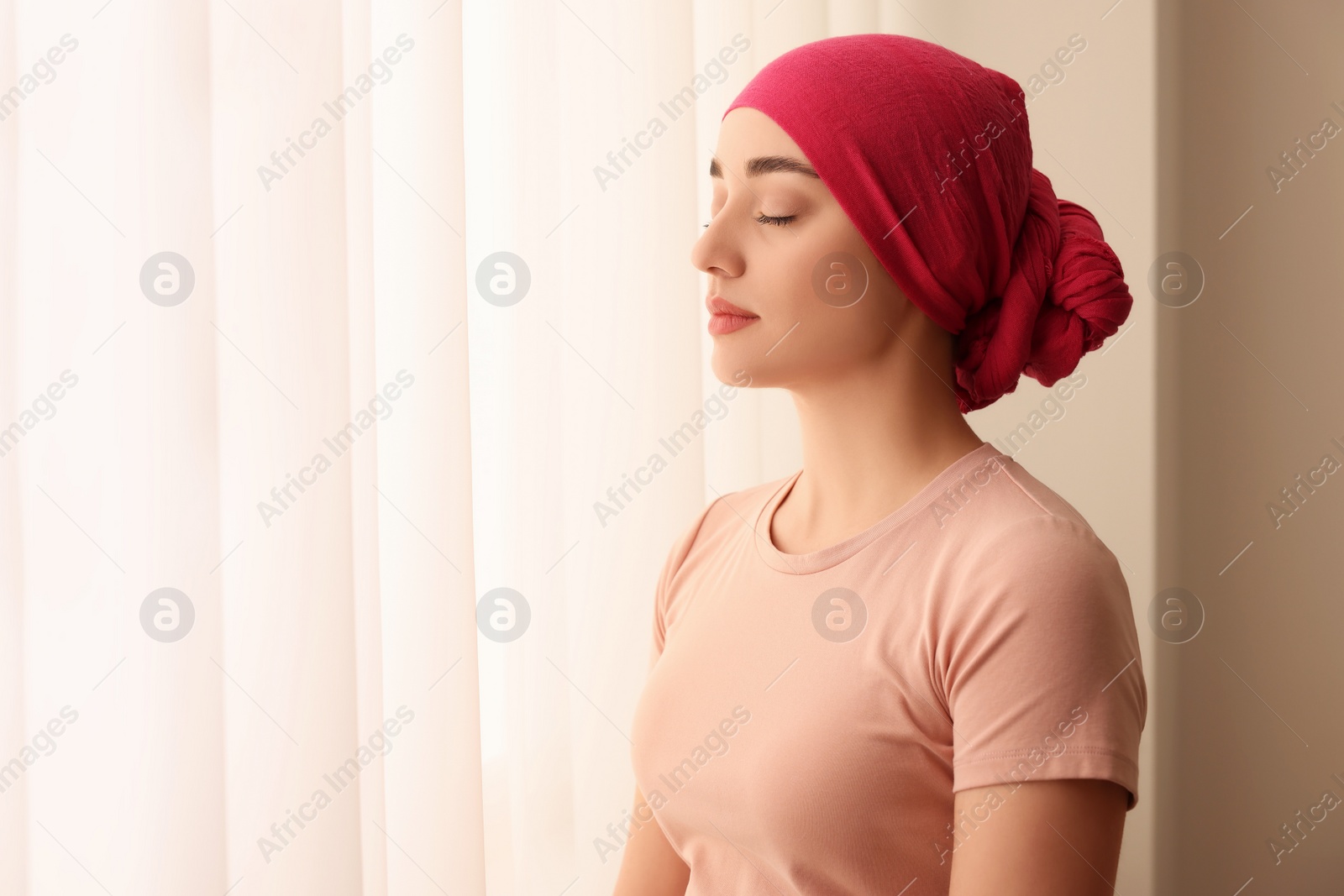 Photo of Cancer patient. Young woman with headscarf near window indoors, space for text