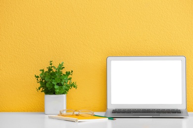 Modern laptop on desk near yellow wall, space for design. Home workplace