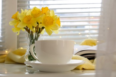 Beautiful yellow daffodils in vase and cup on windowsill