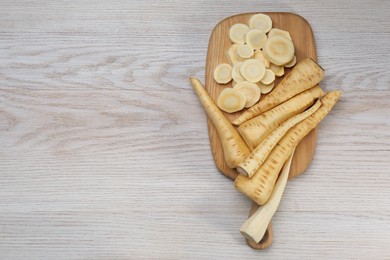 Whole and cut fresh ripe parsnips on white wooden table, top view. Space for text
