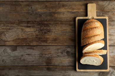 Photo of Board with tasty bread on wooden background, top view. Space for text