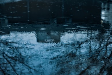 Photo of Rain drops falling down onto puddle outdoors