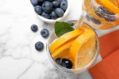 Flat lay composition of delicious orange lemonade with soda water, mint and blueberries on white marble table. Fresh summer cocktail