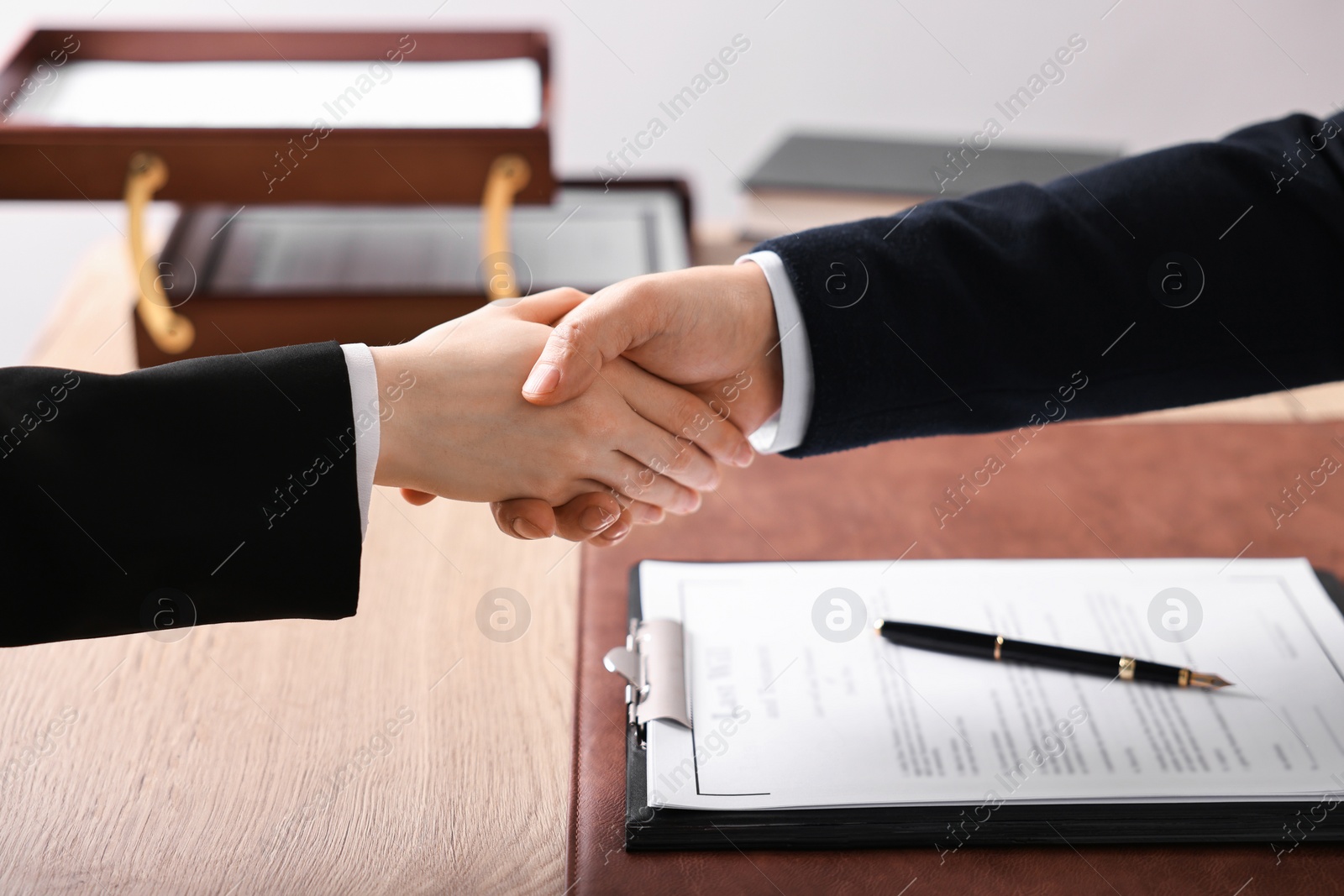 Photo of Notary shaking hands with client at wooden table in office, closeup